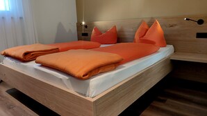 A wooden bed with orange bedding and pillows, a wooden headboard, and a bedside table with a lamp. - Highlight Apartments: Ap. Harmony with garden access, loggia and Mobil Card incl. (Sankt Pauls)