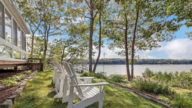 Une vue sur le lac, avec des fauteuils Adirondack, une terrasse en bois et un bâtiment doté de grandes fenêtres.
