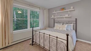 Une chambre à coucher avec un lit, une fenêtre, un ventilateur de plafond et des étagères fixées au mur.