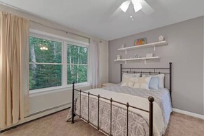 Ein Schlafzimmer mit Bett, Fenster, Deckenventilator und Regalen an der Wand.