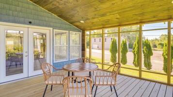 A covered patio with a table and chairs, large windows, and a view of the surrounding landscape.