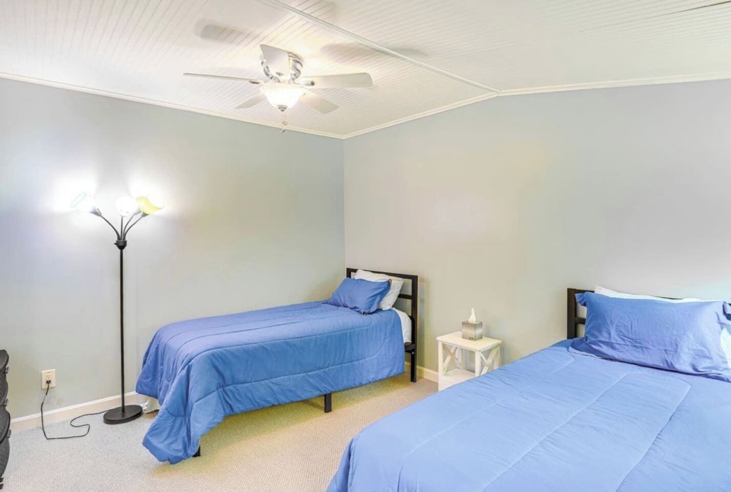 Ein Schlafzimmer mit zwei Betten, einem Deckenventilator, einem Nachttisch mit Lampe und einer Wandsteckdose.