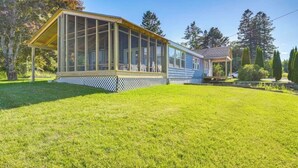 A house with a large glass enclosure, a wooden deck, and a well-maintained lawn.