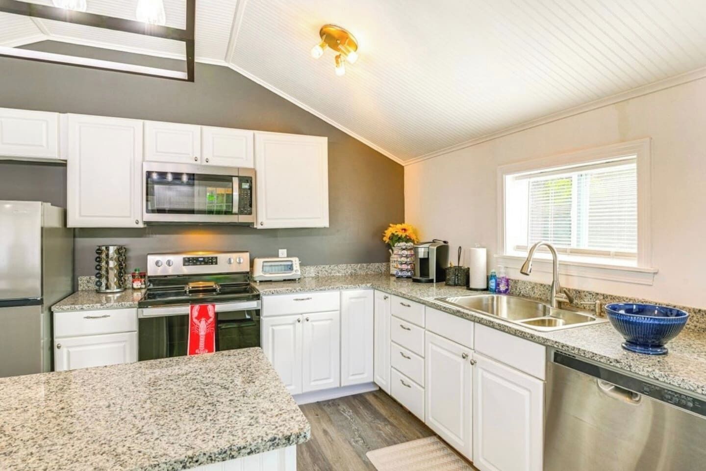 Une cuisine avec des meubles blancs, un four à micro-ondes, une cuisinière, un grille-pain et un évier.