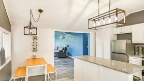 A modern kitchen with white cabinetry, a granite countertop, a stainless steel refrigerator, and a hanging light fixture.