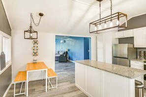 A modern kitchen with white cabinetry, a granite countertop, a stainless steel refrigerator, and a hanging light fixture.