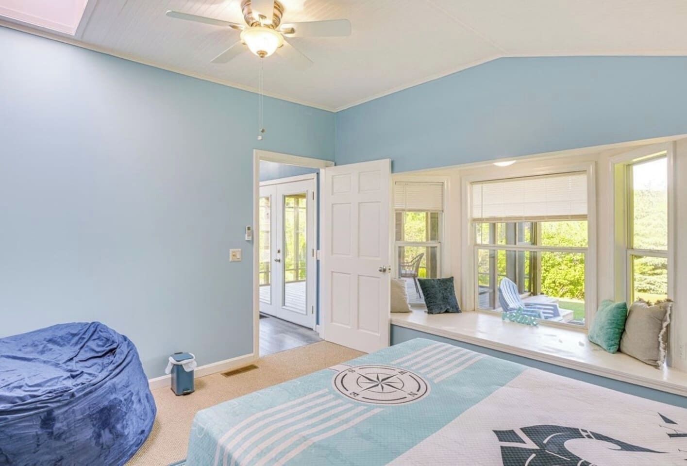 Una habitación con cama, sillón de mimbre, asiento junto a la ventana con vistas y ventilador de techo.