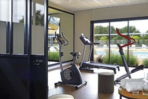 Une salle de sport équipée de matériel d’exercice, une fenêtre donnant sur un espace verdoyant et une petite table avec une serviette et un verre.