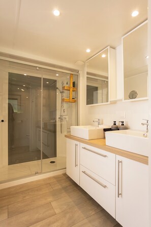 Een moderne badkamer met een douchecabine van glas, twee wasbakken en een grote spiegel.