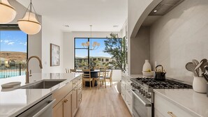 A modern kitchen with a large island, stainless steel appliances, and a view of a pool and mountains. - Barefoot Beach Bungalow 9 Bedroom Home (St. George)