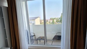 A hotel room with a bed, a sliding glass door to a balcony, and a table with chairs outside. - Roma Apartment luxury flat in  Mamaia Beach by the Black Sea (Năvodari)