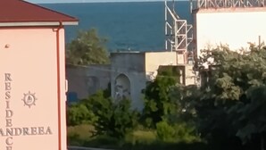 A building with 'RESIDENCE ANDREA' on its facade, a parking lot with several cars, and a view of the sea in the background. - Roma Apartment luxury flat in  Mamaia Beach by the Black Sea (Năvodari)