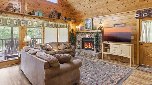 A cozy cabin interior with a fireplace, a television, and a large window overlooking greenery. - Hibernation Station 2 Bedroom Cabin (Sevierville)