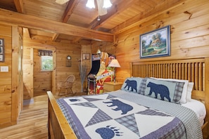 A wooden cabin interior with a bed, a chair, a clock, and a painting on the wall. - Hibernation Station 2 Bedroom Cabin (Sevierville)