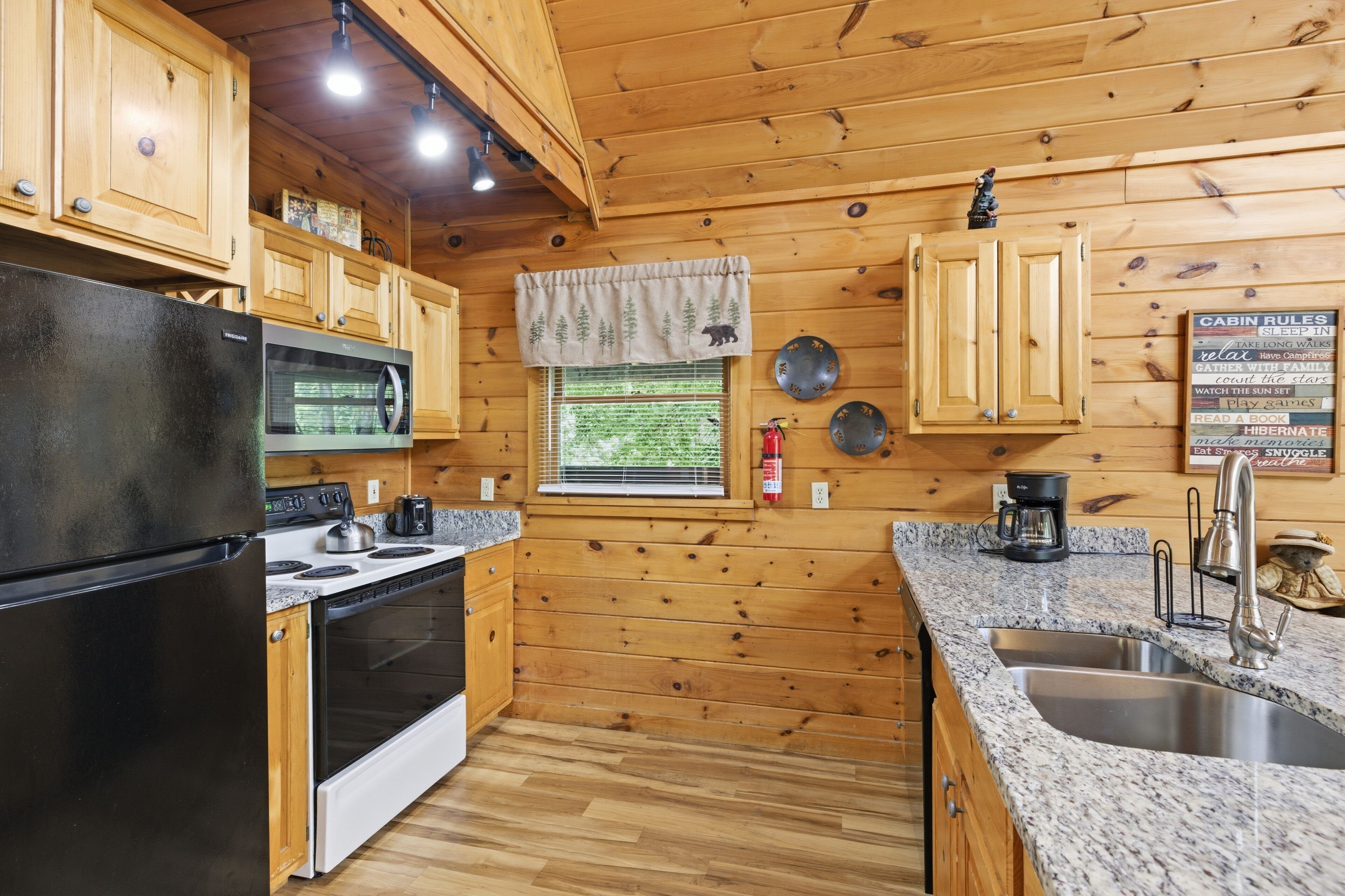 Une cuisine rustique, située dans une cabane en bois, équipée d’un réfrigérateur, d’une cuisinière, d’un four et d’un plan de travail en granit.