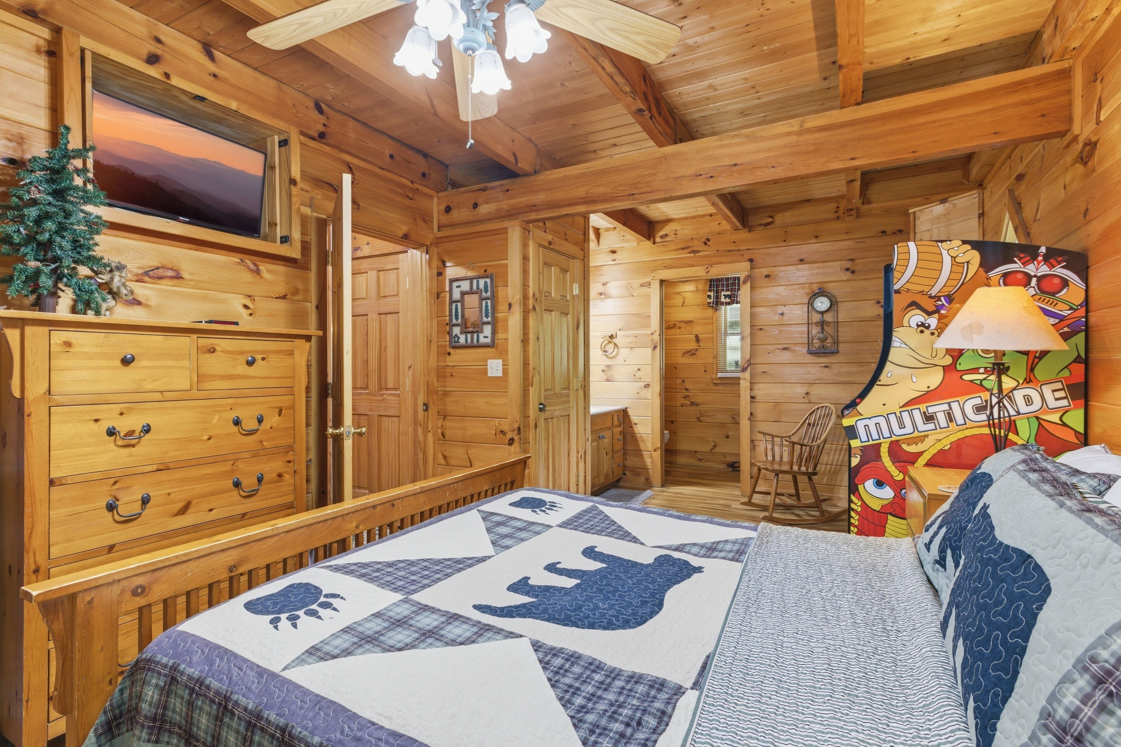 Ein Holzblockhaus-Innenraum mit einem Bett, einem Schminktisch, einem Fernseher, einer kleinen Weihnachtstanne und einem farbenfrohen Wandgemälde.