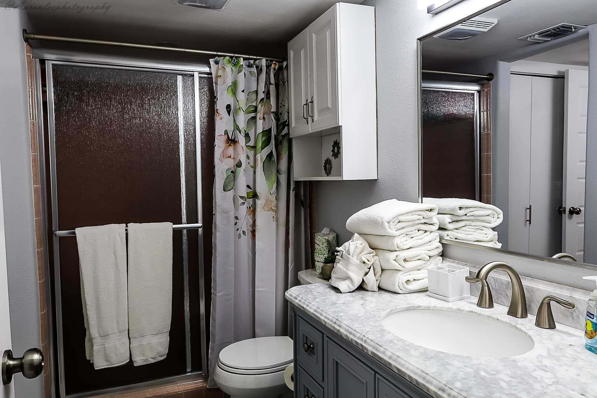 A bathroom with a shower, toilet, sink, and cabinets.