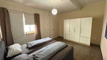 Une chambre à coucher comprenant un lit, une armoire, un luminaire suspendu et une fenêtre avec des rideaux.