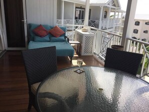 Ein Balkon mit Glastisch, zwei Stühlen, einer Couch mit Kissen und einer Topfpflanze.
