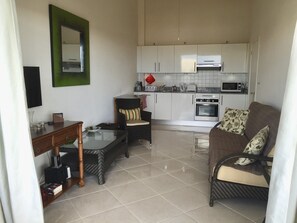A compact living space with a kitchenette, a dining area with wicker furniture, and a flat-screen TV mounted on the wall. - Sea views, one bedroom apartment, Lantana 35 (weston)