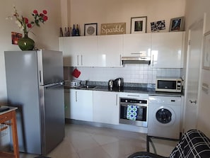 A compact kitchen with white cabinets, a stainless steel refrigerator, a microwave, a toaster, a kettle, and a washing machine. - Sea views, one bedroom apartment, Lantana 35 (weston)