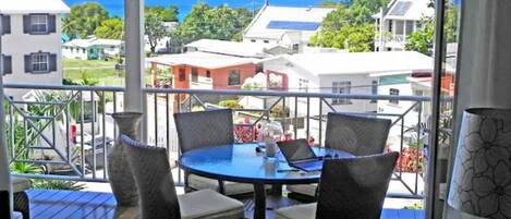 Un balcon avec une table ronde et quatre chaises, donnant sur un quartier résidentiel avec des maisons et offrant une vue sur l’océan.