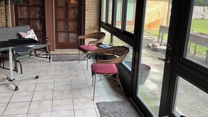 En overdækket terrasse med siddeplads, en dør og udsigt til baghaven.