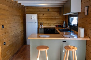 Una cucina compatta con pareti in legno, un frigorifero, un lavello e due sgabelli.