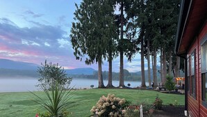 A lakeside property with a well-maintained lawn, a variety of flowering plants, and tall trees. - Delightful 6-bedroom lodge in Monroe perfect for group getaways (Monroe)