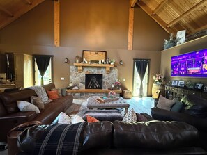 A cozy living room with a stone fireplace, leather sofas, and a flat-screen TV mounted on the wall. - Delightful 6-bedroom lodge in Monroe perfect for group getaways (Monroe)