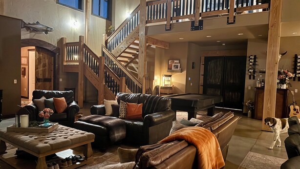 A spacious living area with a pool table, leather sofas, a staircase, and a dog. - Delightful 6-bedroom lodge in Monroe perfect for group getaways (Monroe)