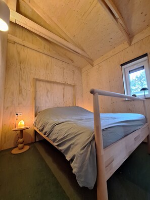 Habitación tipo cabaña de madera con literas, una ventana con vistas y una lámpara de sal sobre una mesa.