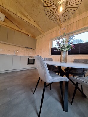 Una cocina moderna con vigas de madera, una mesa de comedor con sillas, un florero con flores y una ventana con persianas.