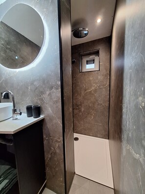 Un baño moderno con pared de mármol, un espejo redondo, un lavabo y un box de ducha.