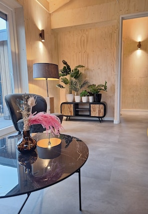 Un salon moderne avec une table basse en verre, un canapé noir, une lampe noire et un meuble en bois orné de plantes.