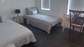 Une chambre avec deux lits, un bureau, une chaise, une fenêtre et une lampe.