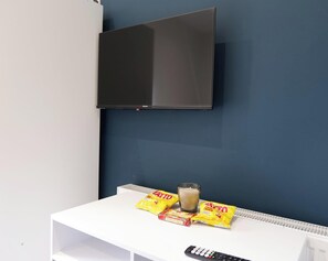 Una habitación con televisión montada, una mesa blanca con aperitivos y un control remoto.