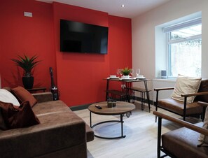 A living room with a red accent wall, a flat-screen TV, a dining table with chairs, a sofa, and a window with a view. - Private Double Room with Ensuite - Walk to City (Derry/Londonderry)