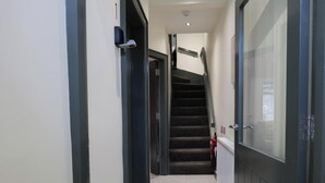 A hallway with a staircase, a fire extinguisher, and a door with a glass panel. - Private Double Room with Ensuite - Walk to City (Derry/Londonderry)