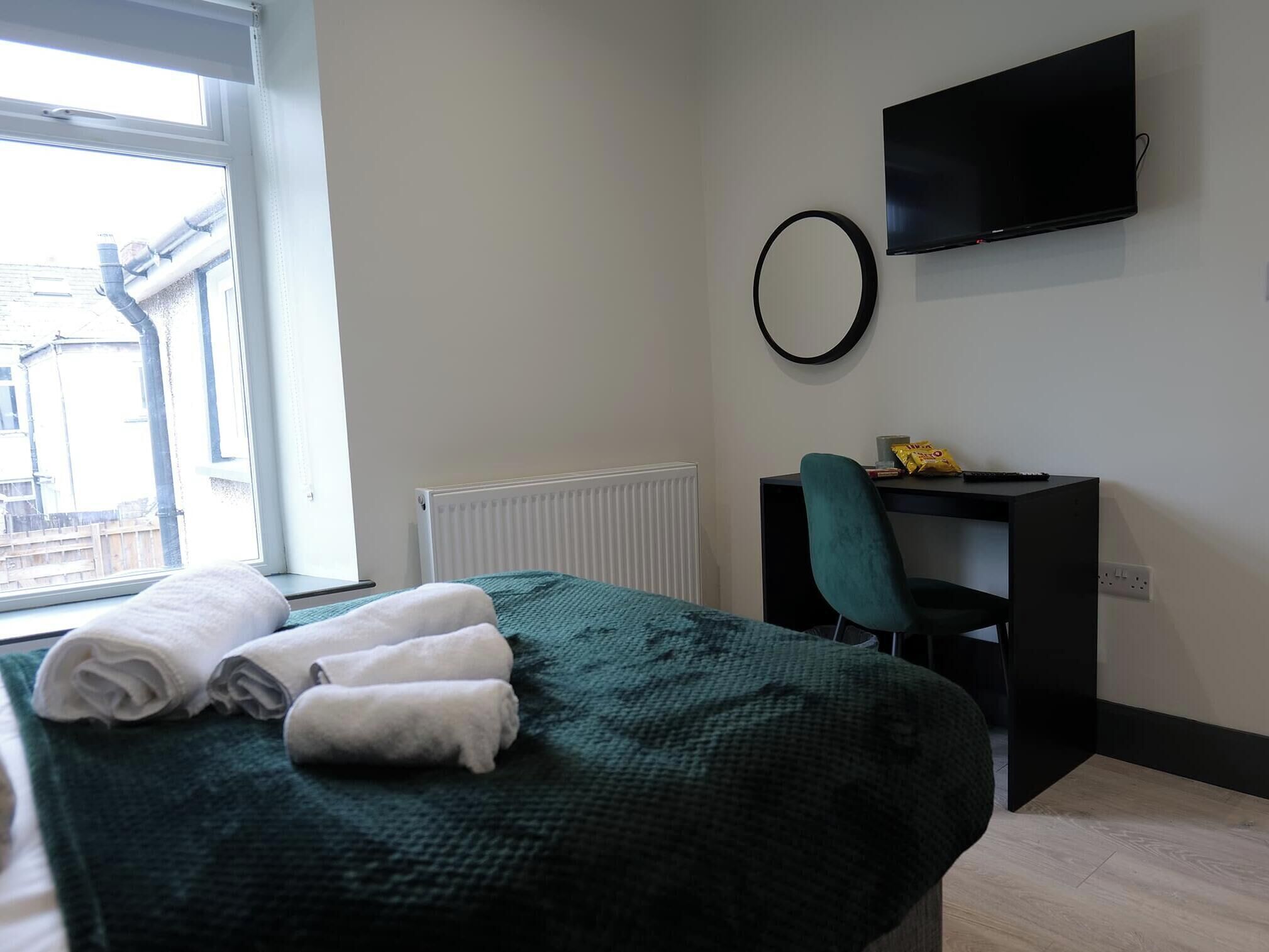 Une chambre d’hôtel comprenant un lit, un bureau avec une chaise, une télévision, une fenêtre et un radiateur.