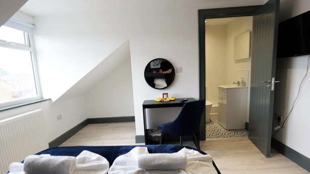 A modern room with a bed, a desk, a chair, a mirror, and a bathroom visible through an open door. - Private Double Room with Ensuite - Walk to City (Derry/Londonderry)