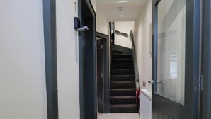 A hallway with a staircase, a fire extinguisher, and a door with a glass panel. - Private Double Room, Shared Bathroom-Walk to City (Derry/Londonderry)