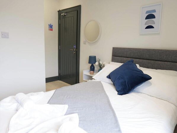A hotel room with a bed, a bedside table with a lamp, a mirror, and a door. - Private Double Room, Shared Bathroom-Walk to City (Derry/Londonderry)