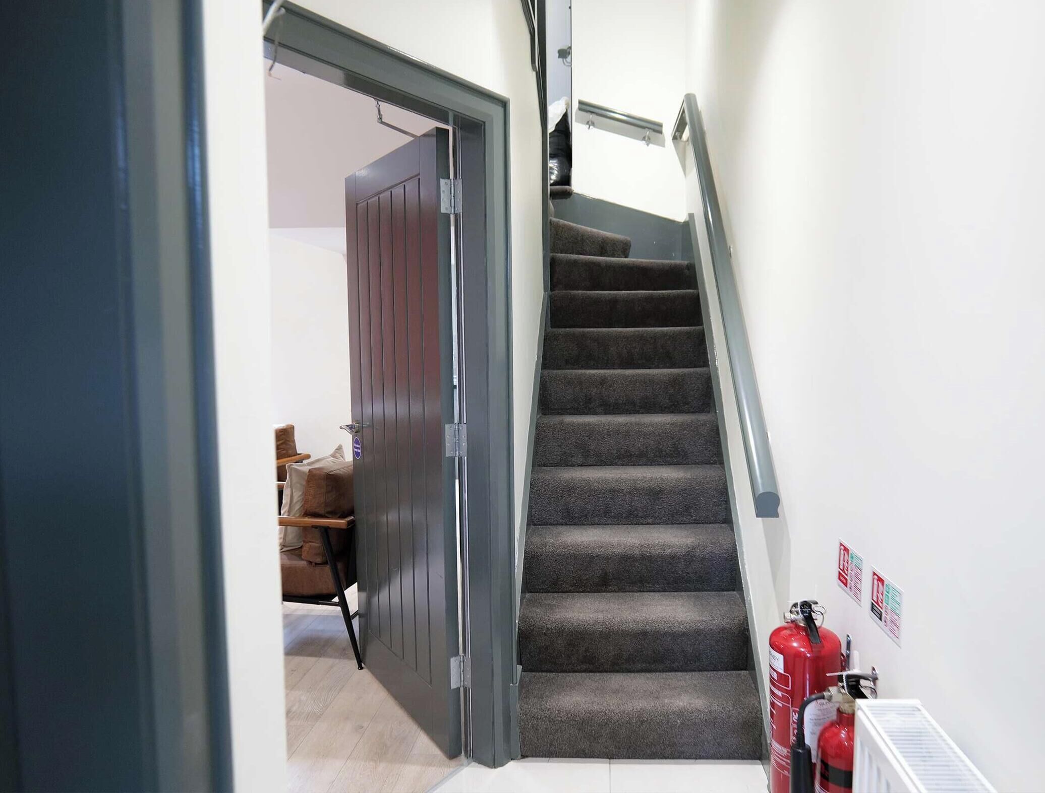 Eine Treppe mit Teppichstufen, ein Feuerlöscher und eine Tür zu einem anderen Raum.