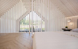 Ein Schlafzimmer mit schrägem Dach, einem Bett, einem Nachttisch und einem Fenster.