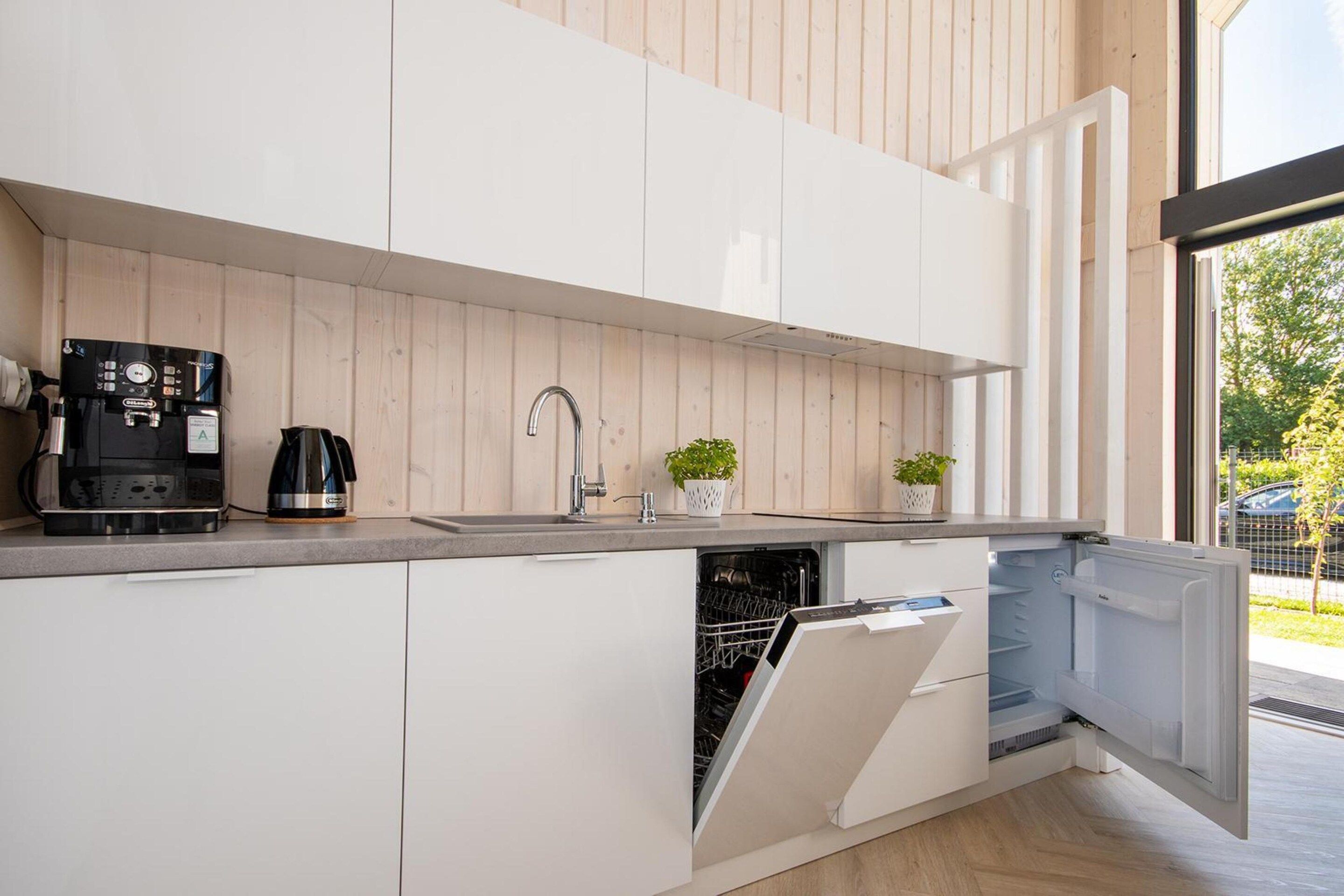 A modern kitchen with white cabinetry, a coffee machine, a sink, and a dishwasher.