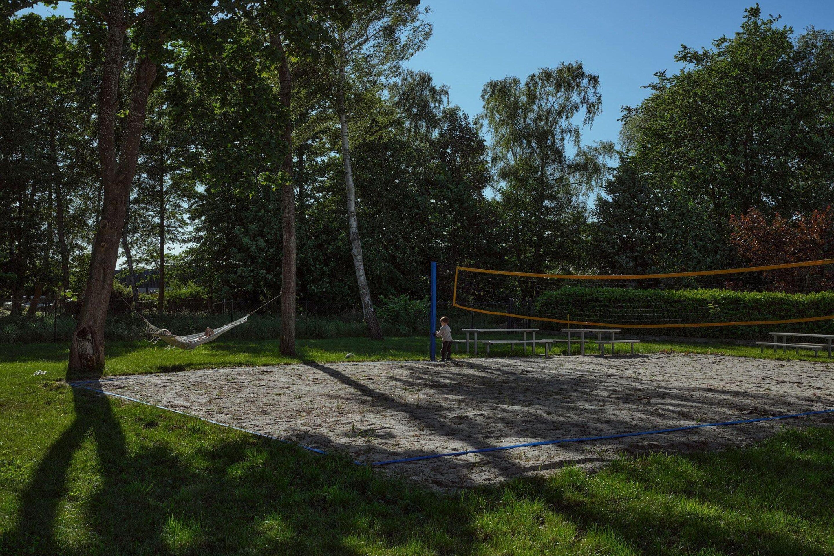 Een volleybalveld met een net, omringd door bomen en gras.