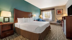 Habitación de hotel con una cama grande, dos lámparas de noche, un escritorio con una silla, un televisor y una ventana con cortinas.