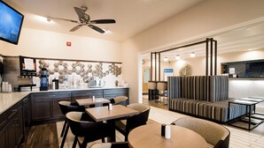 Un vestíbulo de hotel con comedor, un sofá, un televisor y un ventilador de techo.