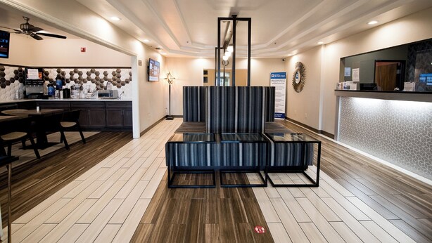Un vestíbulo de hotel con una recepción, una zona de estar con mesas y sillas, una cocina y una pared decorativa con un diseño geométrico.